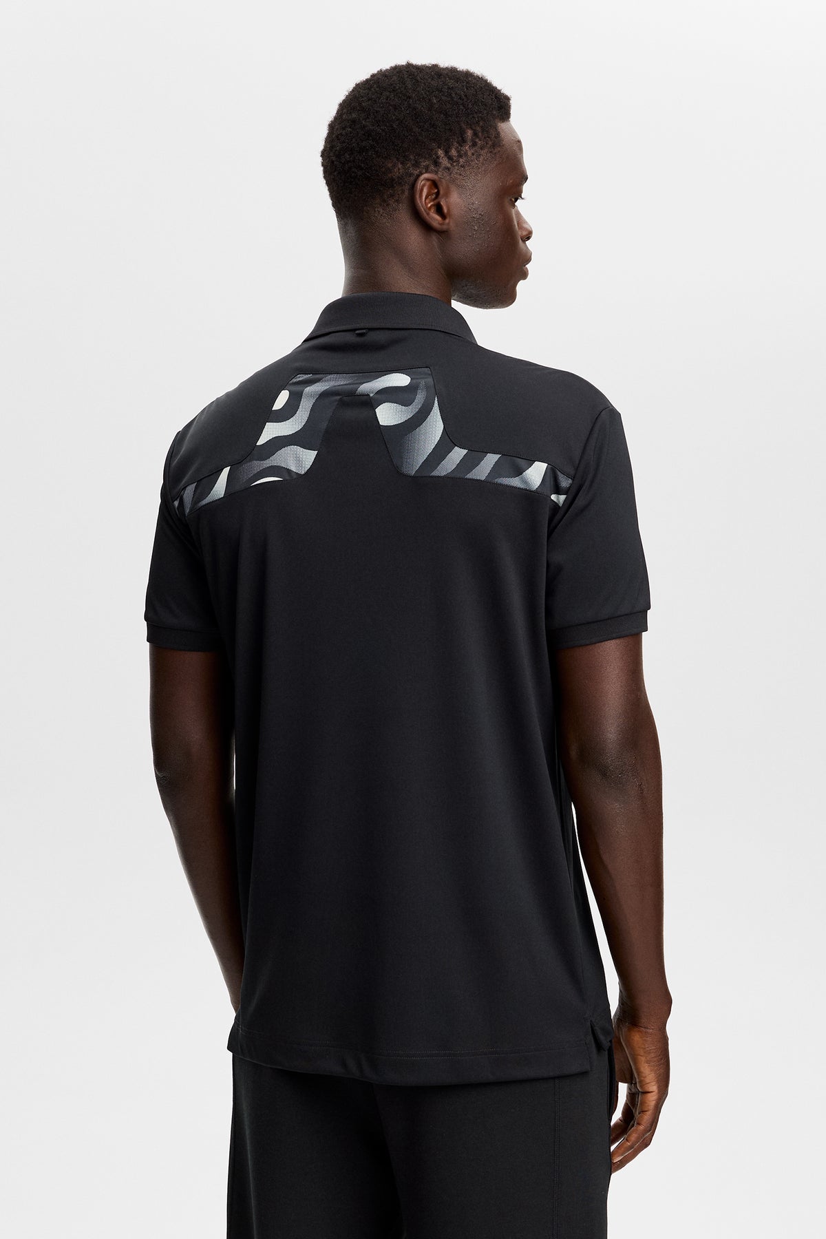 J.Lindeberg KV Print Polo Black – scatto lifestyle sul campo che dimostra la protezione solare UPF 40+